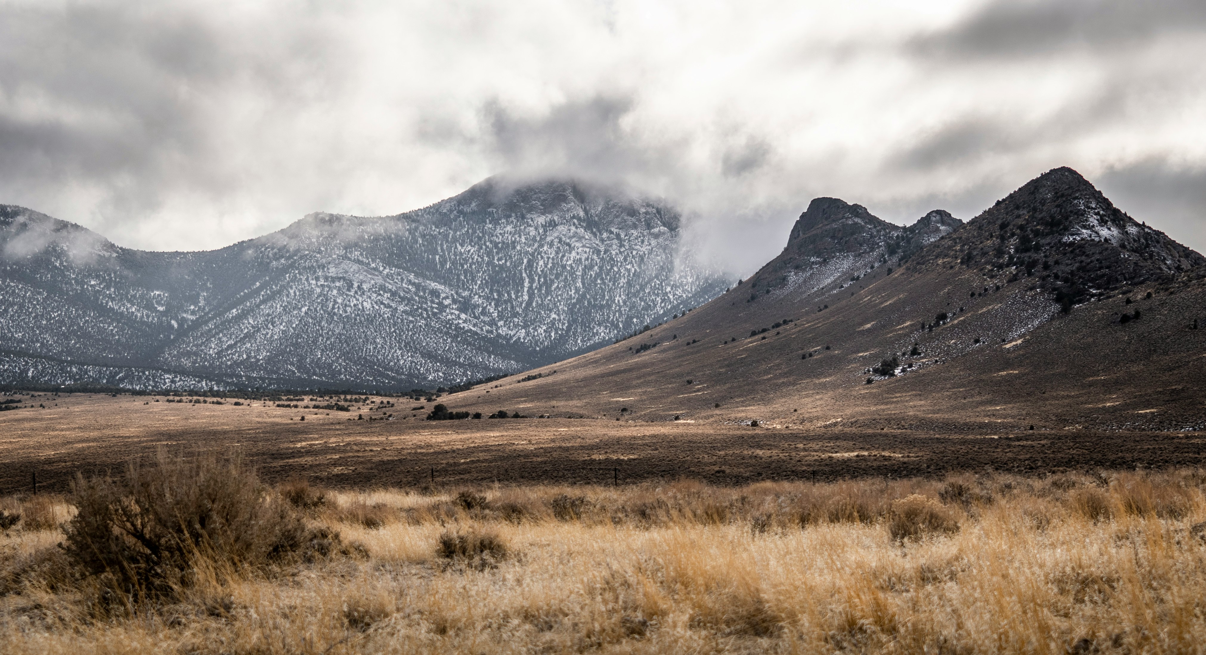 brown grass field near mountain under white clouds during daytime